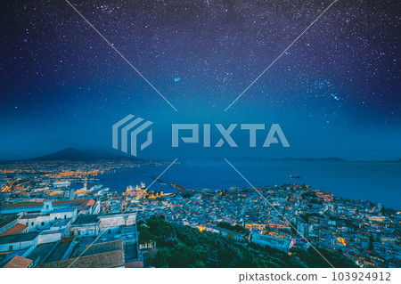 Naples, Italy. Skyline Cityscape In Evening Lighting. Tyrrhenian Sea And Landscape With Volcano Mount Vesuvius. City In Night Illuminations. Bold Bright Blue Azure Night Starry Sky With Glowing Stars Naples, Italy. Skyline Cityscape In Evening Lighting. Tyrrhenian Sea And Landscape With Volcano Mount Vesuvius. City In Night Illuminations. Bold Bright Blue Azure Night Starry Sky With Glowing Stars 103924912