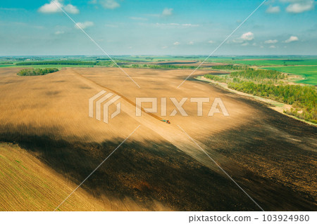 Aerial View. Tractor Plowing Field In Spring Season. Beginning Of Agricultural Spring Season. Cultivator Pulled By A Tractor In Countryside Rural Field Landscape 103924980