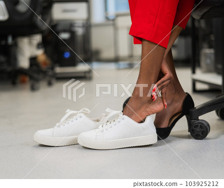 African woman changing from high heels to sneakers in the office. Tired legs. African woman changing from high heels to sneakers in the office. Tired legs. 103925212