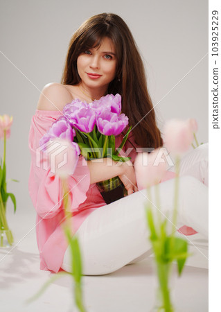 beautiful brunette woman with long hair sits on the floor with vases of flowers  103925229