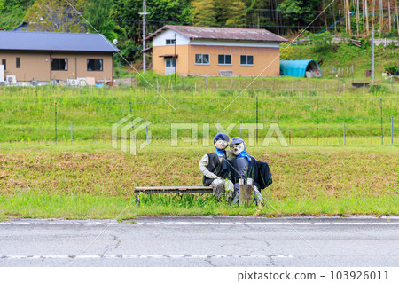 Two scarecrows sitting together on a bench on a country road Two scarecrows sitting together on a bench on a country road 103926011