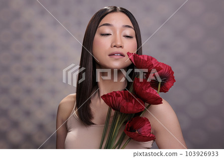 Young attractive asian woman holding poppy bunch, looking at red flower. Beautiful fashion model posing with bright summer blossoms branch, standing with blooming plants bouquet Young attractive asian woman holding poppy bunch, looking at red flower. Beautiful fashion model posing with bright summer blossoms branch, standing with blooming plants bouquet 103926933