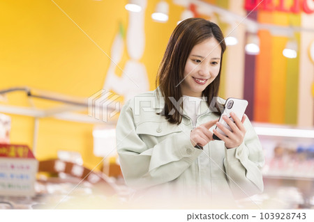 A young woman in work clothes operating a smartphone at a supermarket A young woman in work clothes operating a smartphone at a supermarket 103928743