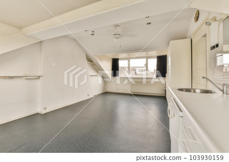 an empty room with white walls and black flooring on the right, there is a large window to the left an empty room with white walls and black flooring on the right, there is a large window to the left 103930159