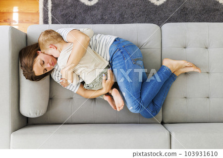 Mother embraces her cute little son while laying together on the couch 103931610