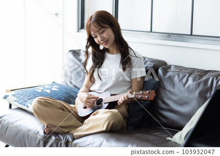 Woman playing ukulele in her room Woman playing ukulele in her room 103932047