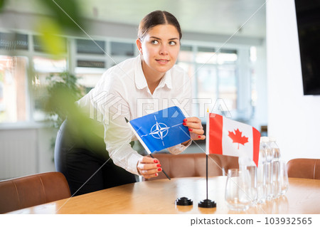 Young lady sets miniatures flags of Canada and NATO before international negotiations 103932565