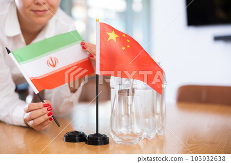 Unrecognizable girl sets midget flags of China and Iran before international negotiations 103932638