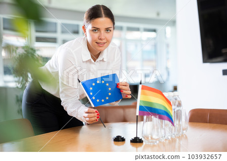 Young woman puts EU and LGBT flags on table in office 103932657