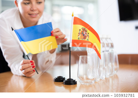 Young woman puts flags of Ukraine and Spain on table in office Young woman puts flags of Ukraine and Spain on table in office 103932781