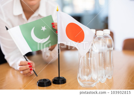 Little flag of Japan on table and flag of Pakistan put next to it by young woman Little flag of Japan on table and flag of Pakistan put next to it by young woman 103932815