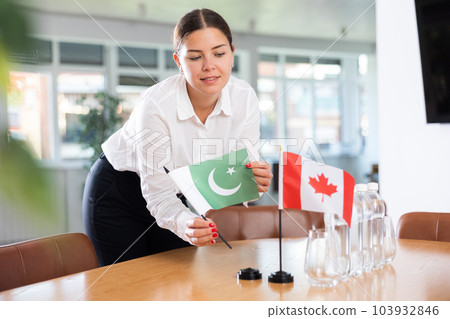 Young lady sets miniatures flags of Canada and Pakistan before international negotiations 103932846