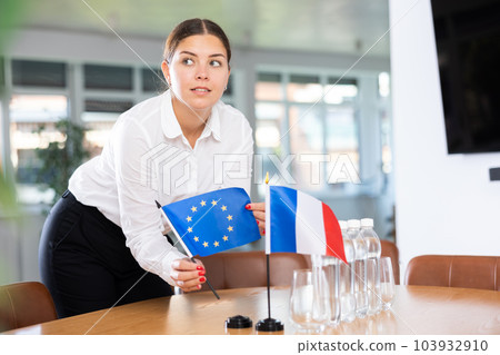 Female secretary places flags of the France and European Union flag on the table before negotiations of top political figures 103932910
