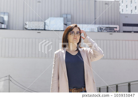 Portrait Confident Mature 40 yo Business Woman, Manager. Industrial Construction, Factory on Background. Caucasian Burnette Female In Sunglasses Looks Away, Wears Pink Jacket, Blue Shirt. Horizontal. 103933847