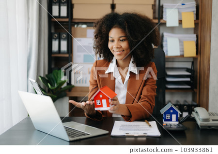 Young real estate agent worker working with laptop and tablet at table in office and small house beside it. 103933861