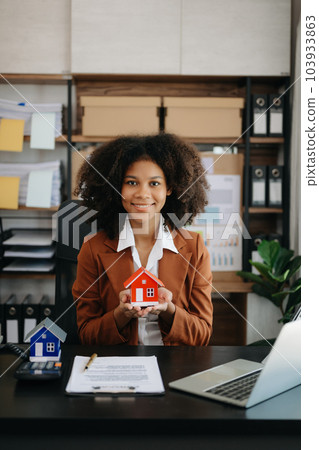 Young real estate agent worker working with laptop and tablet at table in office and small house beside it. 103933863