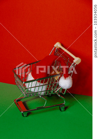 Santa hat in shopping trolley on isometric red green background. Online shopping holiday concept Copy space for your text. Mock up for advertisement. Holiday Christmas composition. Minimalistic Santa hat in shopping trolley on isometric red green background. Online shopping holiday concept Copy space for your text. Mock up for advertisement. Holiday Christmas composition. Minimalistic 103934056