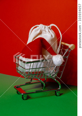 Santa hat in shopping trolley on isometric red green background. Online shopping holiday concept Copy space for your text. Mock up for advertisement. Holiday Christmas composition. Minimalistic Santa hat in shopping trolley on isometric red green background. Online shopping holiday concept Copy space for your text. Mock up for advertisement. Holiday Christmas composition. Minimalistic 103934057