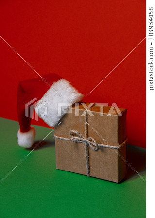 Santa hat on paper gift box present on green background. Copy space for your text. Mock up for advertisement. Holiday Christmas composition Santa hat on paper gift box present on green background. Copy space for your text. Mock up for advertisement. Holiday Christmas composition 103934058