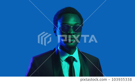 Neon people. Gentleman look. Elegant style. Portrait confident business man in party suit tie glasses on blue color light copy space background. Neon people. Gentleman look. Elegant style. Portrait confident business man in party suit tie glasses on blue color light copy space background. 103935338
