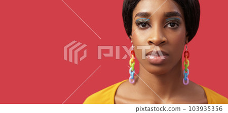 Lgbt portrait. Diversity colors. Equality right. Confident proud woman face bright makeup rainbow earrings on pink empty space background. 103935356