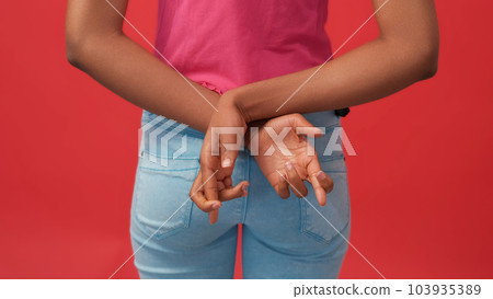 Crossed fingers. Liar sign. Fake promise. Unrecognizable dishonest woman hiding hands behind back isolated on red free space background. 103935389