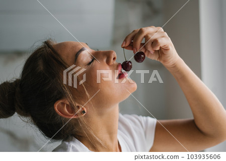 Pretty woman with beautiful plump lips touches cherries to them and wants to eat a berry 103935606