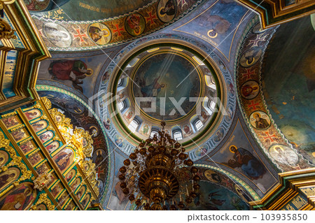 Beautiful dome in an orthodox cathedral, church. Beautiful Christian murals. The sun's rays illuminate the dome beautifully. Beautiful mural with Jesus Christ. Apostles and icons. 103935850