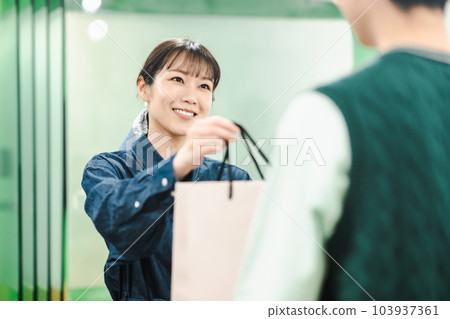 Female clerk handing products to customers at a shop Female clerk handing products to customers at a shop 103937361