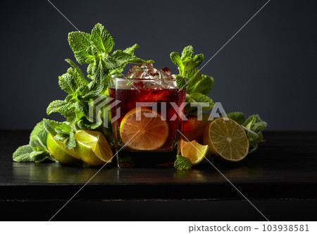 Cocktail Cuba Libre with rum, cola, mint, and lime on a black background. Cocktail Cuba Libre with rum, cola, mint, and lime on a black background. 103938581