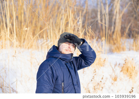 Male man looking at camera, holding hand over his eyes on high dry reeds, snow. European caucasian white smiling man. Winter hiking, leisure activities. Male man looking at camera, holding hand over his eyes on high dry reeds, snow. European caucasian white smiling man. Winter hiking, leisure activities. 103939196