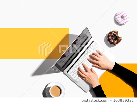 Person using a laptop computer with a donut and a cup of coffee Person using a laptop computer with a donut and a cup of coffee 103939355