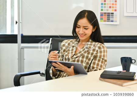 Smiling young woman in trendy suit using digital tablet, working on design project at creative office Smiling young woman in trendy suit using digital tablet, working on design project at creative office 103939860