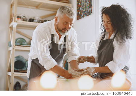 Mutual creative work. Adult elegant couple in casual clothes and aprons. People creating a bowl on a pottery wheel in a clay studio. 103940443
