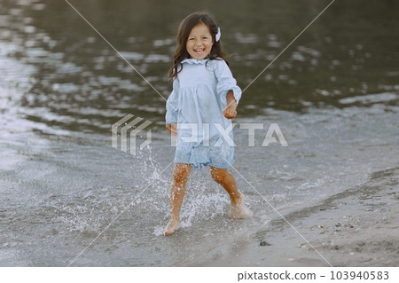 Little girl on the river. Girl splashes water. Girl in a blue dress. 103940583