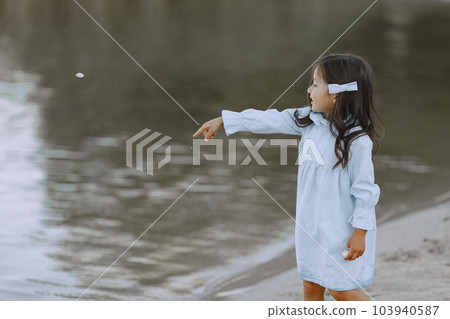 Little girl on the river. Girl splashes water. Girl in a blue dress. Little girl on the river. Girl splashes water. Girl in a blue dress. 103940587