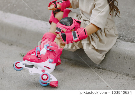 Child in a summer park. Kid in a pink helmet. Little girl with a roller. Child in a summer park. Kid in a pink helmet. Little girl with a roller. 103940624
