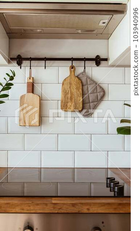 Kitchen brass utensils, chef accessories. Hanging kitchen with white tiles wall and wood tabletop.Green plant on kitchen background Kitchen brass utensils, chef accessories. Hanging kitchen with white tiles wall and wood tabletop.Green plant on kitchen background 103940996