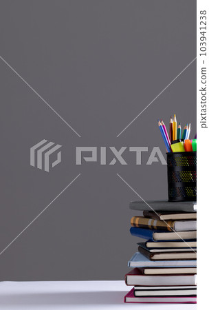 Stack of books and notebooks with pencil container on top and copy space on grey background 103941238