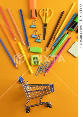 Close up of miniature shopping trolley with school materials on orange background 103941372