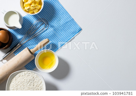 Directly above shot of flour, butter, milk, egg, yolk in bowls with whisk, rolling pin and napkin 103941781