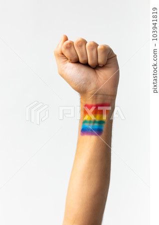 Close up of hand of biracial man clenching fist with rainbow flag on white background 103941819