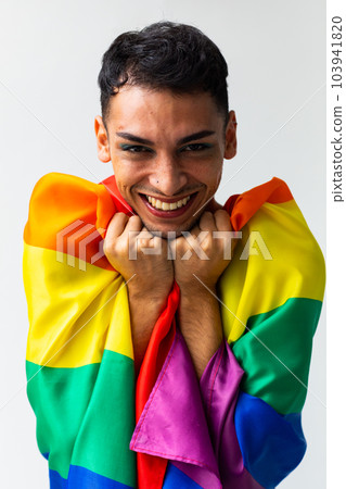 Portrait of happy biracial transgender man holding rainbow flag on white background 103941820