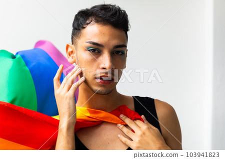 Portrait of biracial transgender man holding rainbow flag on white background Portrait of biracial transgender man holding rainbow flag on white background 103941823