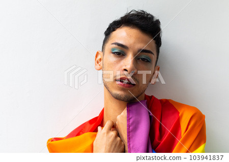 Portrait of biracial transgender man holding rainbow flag on white background 103941837
