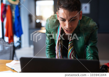 Biracial transgender fashion designer leaning on desk and using laptop 103941844