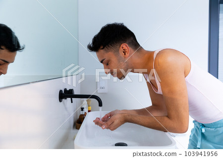 Biracial transgender man washing face in bathroom Biracial transgender man washing face in bathroom 103941956