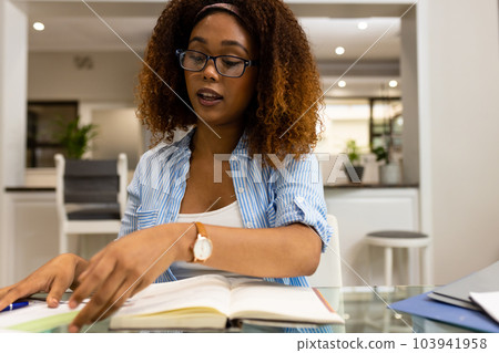 Biracial woman in glasses working at home, talking and looking at documents during video call Biracial woman in glasses working at home, talking and looking at documents during video call 103941958