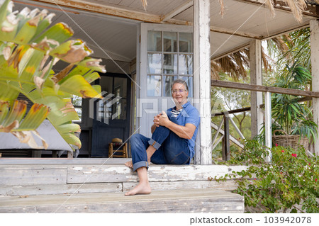 Portrait of caucasian senior man dressed in casuals sitting on steps outside wooden cottage 103942078