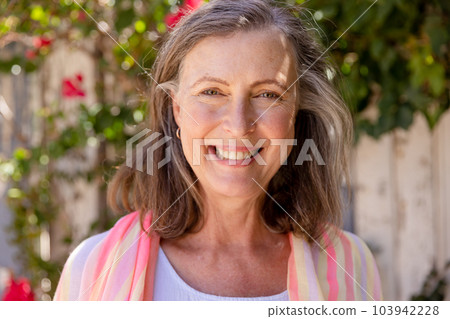 Close-up portrait of beautiful caucasian senior woman smiling at camera against plants, copy space Close-up portrait of beautiful caucasian senior woman smiling at camera against plants, copy space 103942228